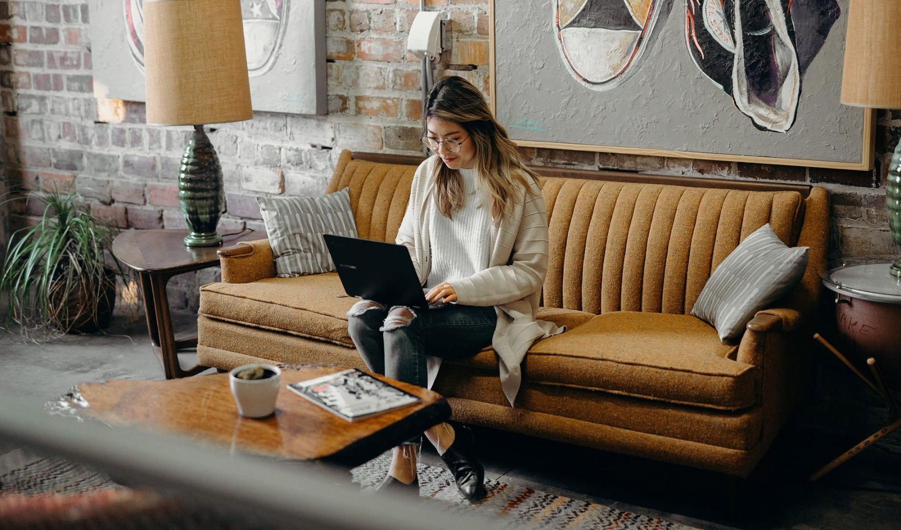 a woman sitting on a couch working on a laptop