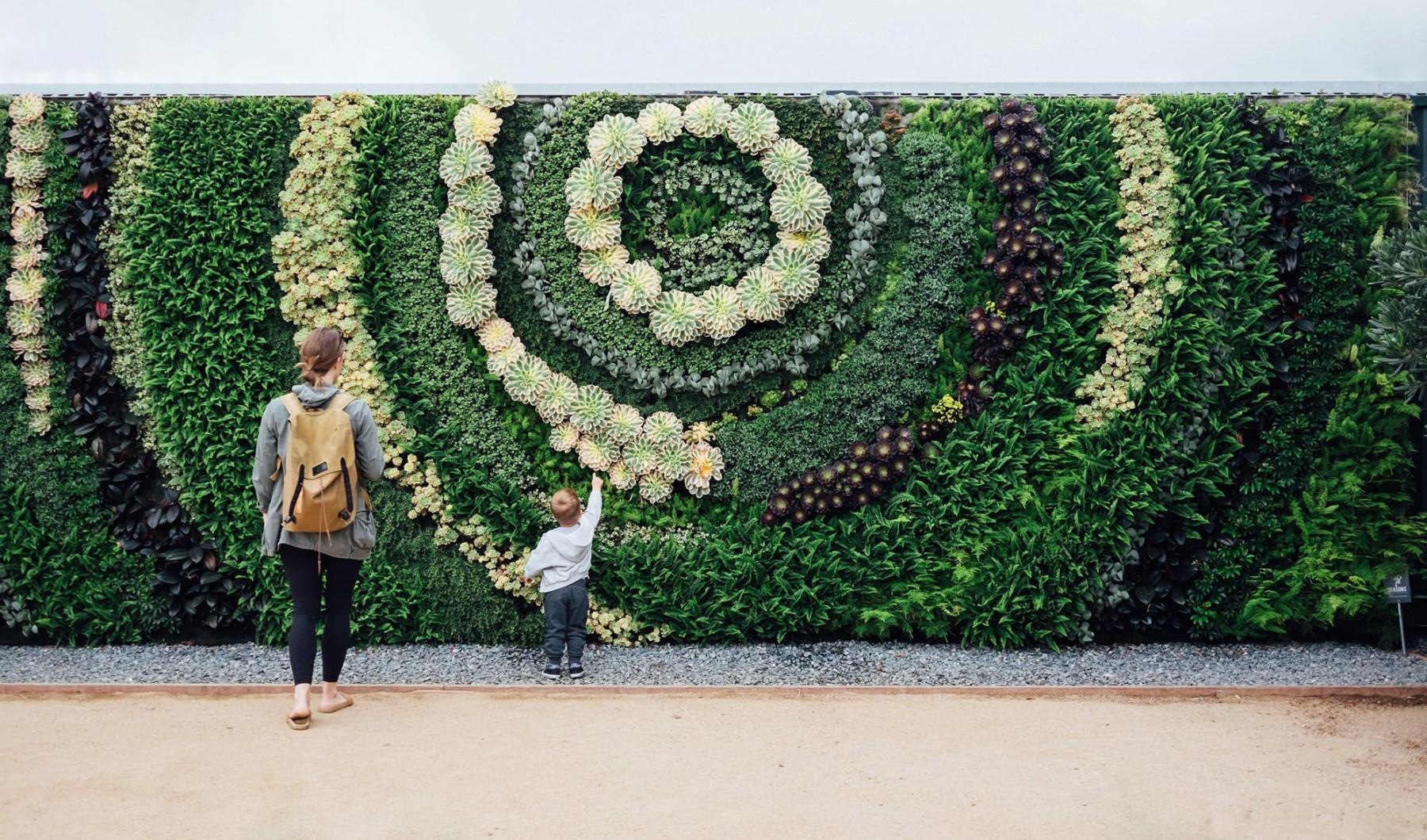 mother and child standing in front of a mural made of plants